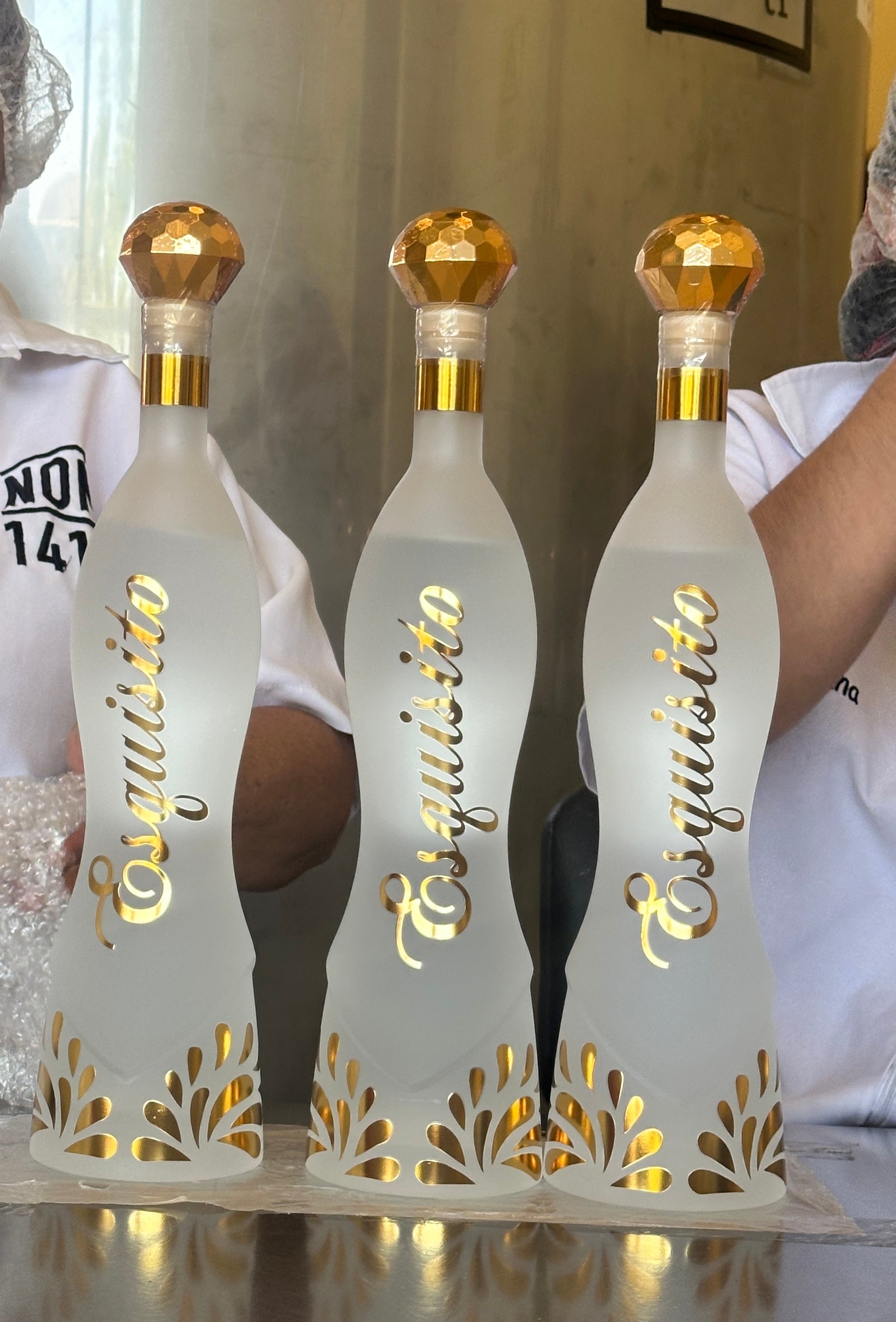 Three 'Esquisito' bottles with gold caps on a decorative stand.