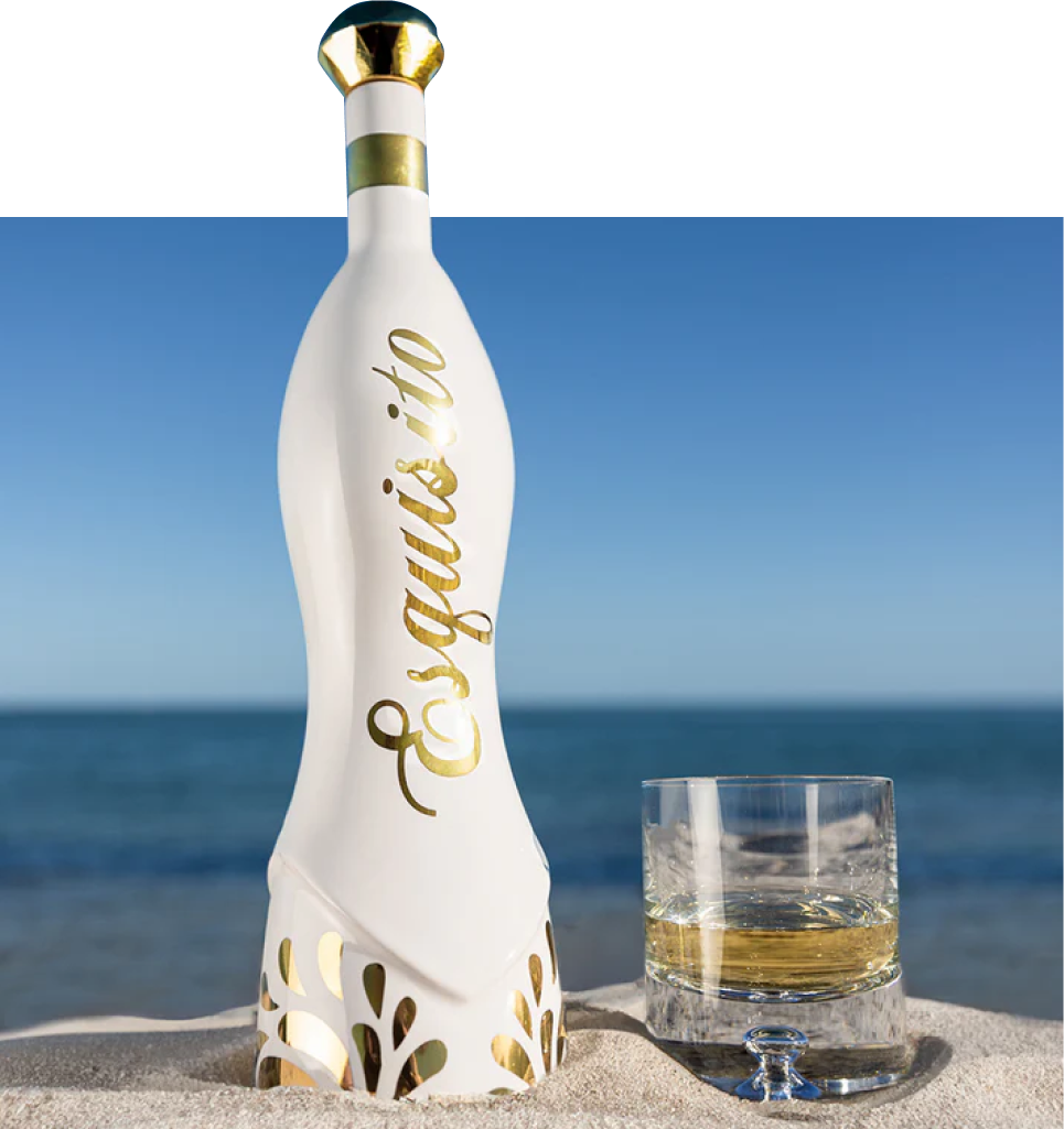 Esquisito Premium Agave Tequila bottle with gold accents on a beach